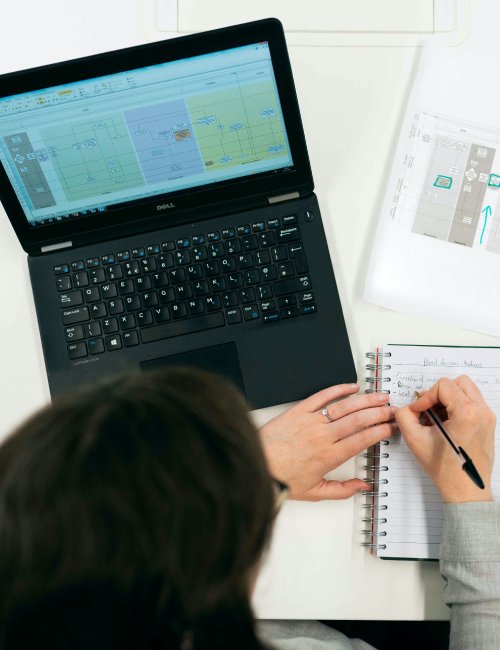 A person writing in a notebook next to a laptop.